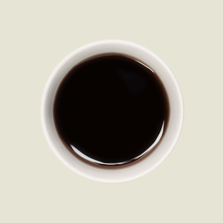 Tasse Pu Erh Mini Tuo Cha von oben, mit einer tiefen, erdigen Teefarbe, die die kräftigen und komplexen Aromen dieses Tees widerspiegelt.
Pu Erh Mini Tuo Cha cup from above, showcasing the deep earthy tea color that reflects the strong and complex flavors of this tea.