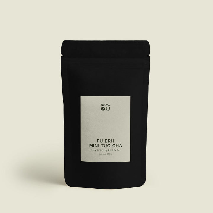 Verpackung des Pu Erh Mini Tuo Cha Tees mit Etikett, das die Tradition und die fermentierten Aromen des Yunnan Pu Erh Tees in handgepressten Nestern darstellt.
Packaging of Pu Erh Mini Tuo Cha Tea with label, showcasing the tradition and fermented flavors of Yunnan Pu Erh tea in pressed mini nests.